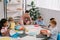 male teacher and multiracial preschoolers sitting at table with colorful papers