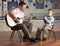 Male Teacher Playing Guitar With Pupil In Classroo