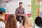 Male Teacher Reading Story To Group Of Elementary Pupils In School Classroom