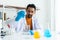 A male teacher in white lab coat with rubber gloves with many laboratory tools on shelves and table. Using pipette