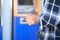 A male tourist in a long-sleeved striped shirt with a camera stands in front of an ATM, happily waiting to withdraw cash for a