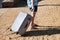 Male tourist and traveler walking and pull his traveled suitcase on sandy beach of hotel resort. Handsome man on vacation.