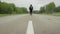 A male tourist walks along the center of the asphalt road in windy rainy weather. Hitchhiking travel concept, tourism