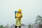 Male tourist in a yellow raincoat stands on top of a mountain in rainy weather against a background of clouds and uses a