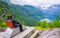 Male tourists sitting on the Queen Sony Chair at the Flydalsjuvet Viewpoint. The Geiranger village and Geirangerfjord landscape.