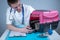 Male veterinarian takes notes on health check of gray Scottish Straight kitten in animal carrier on examination table in