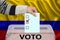 Male voter drops a ballot in a transparent ballot box against the backdrop of the Colombia national flag, concept of state