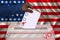 Male voter drops a ballot in a transparent ballot box against the background of the national flag of America, concept of state