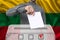 Male voter drops a ballot in a transparent ballot box against the background of the national flag of Lithuania, concept of state