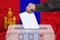 Male voter drops a ballot in a transparent ballot box on the background of the national flag of Mongolia, concept of state