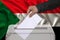 Male voter drops a ballot in a transparent ballot box on the background of the national flag of Sudan, concept of state elections