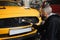 Male worker in gloves washes car radiator grille of luxury yellow car with special brush and soap