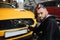 Male worker in gloves washes car radiator grille of luxury yellow car with special brush and soap