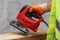 Male worker holds a close-up jigsaw electric in his hands against the background of a concrete wall.