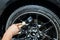 A male worker washes a black car with a special brush for cast wheels and scrubs the surface to shine in a vehicle detailing