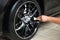 A male worker washes a black car with a special brush for cast wheels and scrubs the surface to shine in a vehicle detailing