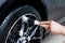 A male worker washes a black car with a special brush for cast wheels and scrubs the surface to shine in a vehicle detailing