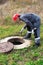 A male working plumber in overalls shines a flashlight into a water well. Inspection and repair of plumbing systems