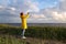 Male in yellow raincoat wear red hat standing on the beach at wooden path, looks at dramatic cloudy sky and takes photo on