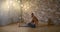 Male yogi is training alone indoors, sitting on floor of room in evening, lying torso