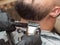 Males beard cutting with clipper and black comb, close up view. Stylistd hands in black rubber gloves. Master at work in