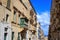 Malta, Valletta, traditional sandstone buildings with colorful wooden windows on balconies. Blue sky with clouds and sea backgroun