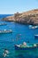 Maltese boats and swimming people in water of Wied Zurrieq Fjord