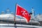 Maltese old flag on pole on ferry`s stern. Ongoing cruise to islands. Blue sky background, close up view