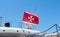 Maltese old flag on pole on ferry`s stern. Ongoing cruise to islands. Blue sky background, close up view