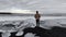 Man admiring the view of sea with foamy waves crashing on a black sandy beach with small icebergs