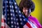 Man with Afro hairstyle having fun, holding american flag, rejoicing, celebrating national holiday.