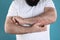Man with allergy symptoms scratching forearm on color background