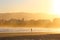 A man alone walking on the beach sand at dusk. Golden sunset light over the entire environment