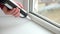 A man applies a sealant to the seam between the window and the sill from a tube of silicone sealant caulking with gun.