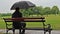 Man approaching bench and sit while raining.