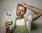 Man in apron with kitchen cloth and detergent spray feeling overwhelmed and bored doing domestic housework of cleaning and washing