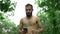 A man of Arab appearance with a beard and without a T -shirt runs in a park with a smartphone in his hand. Shooting of