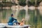 Man as a dog owner and his friend beagle dog are sitting on the wooden pier on the mountain lake and enjoying the landscape during