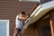 Man attaches gutter on roof of porch