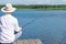 Man, on the background of nature, sits on the pier with a fishing rod in his hands, view from the back