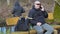 Man with backpack and fishing rod sitting on the bench and talking on phone