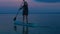 A man with a backpack floats on a SUP board on the smooth water of the lake at sunset in the evening