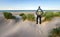 Man with Backpack hiking in beautiful windy coastal dune marram grass towards beach of North Sea in soft evening sunset