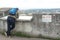 Man with backpack in rear view leaning over concrete barrier with warning sign to prevent tip over.