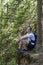 Man with a backpack sitting in a coniferous forest on a cliff. Vertical frame