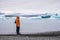 Man with a backpack standing on the beach against the background of an glacier lagoon with icebergs and views of the snow-capped