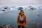 Man with a backpack standing on the beach against the background of an glacier lagoon with icebergs and views of the snow-capped