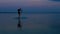 A man with a backpack on a SUP board swims in the lake at dusk in the evening