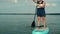 A man with a backpack on a SUP board swims in the lake before sunset against the background of a sky with clouds