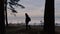 Man with a backpack walks along the trees along the shore in the background of the bay.